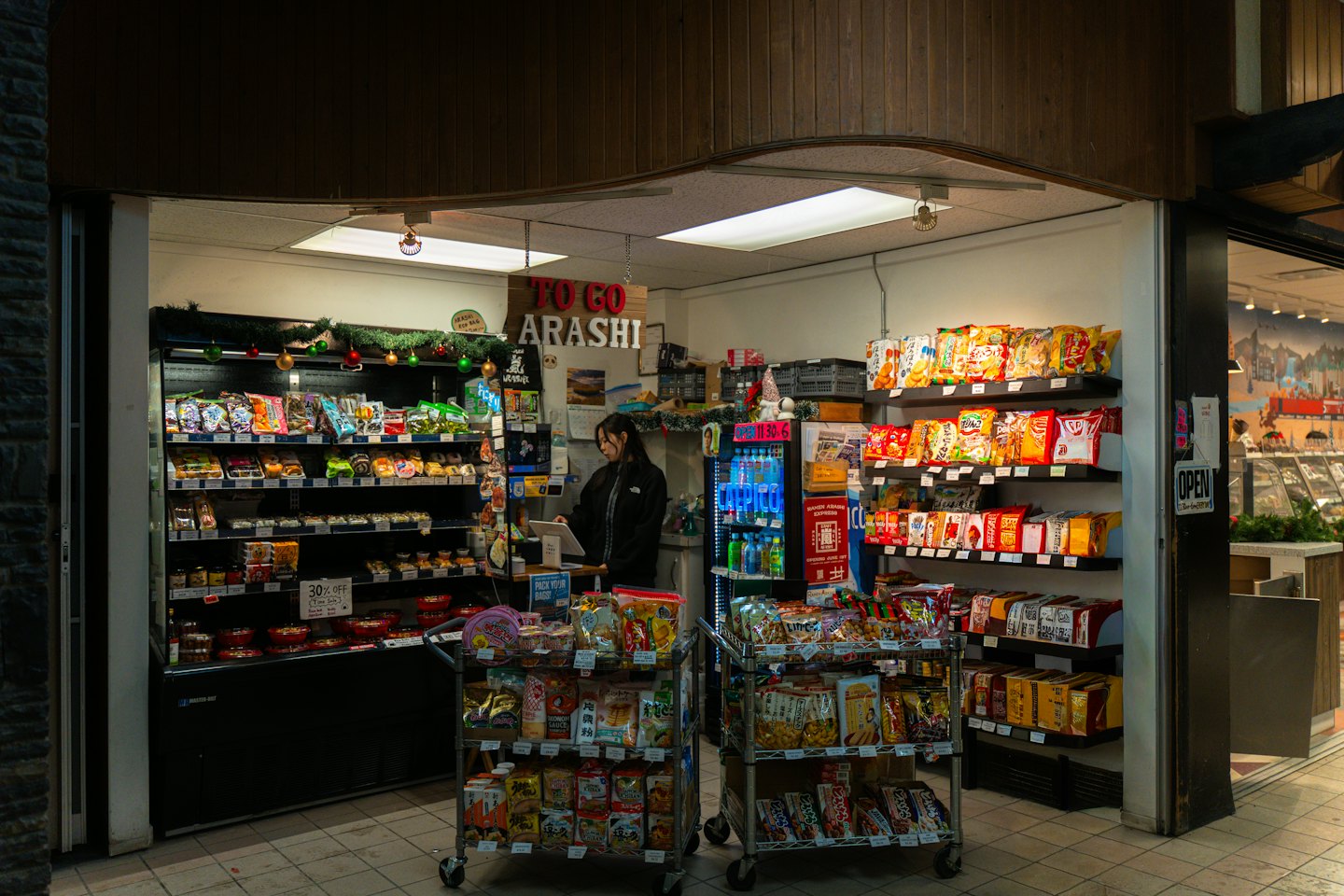 Woman operates tablet behind counter in a busy convenience store.